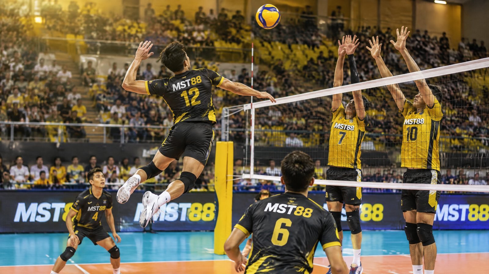 ทีมวอลเลย์บอลหญิงในชุดสีดำเหลืองแดงฉลองแต้มในสนามในร่มที่เต็มไปด้วยผู้ชม